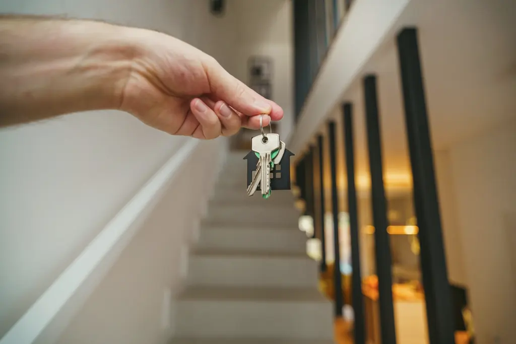 A hand holding a set of house keys at the foot of a staircase